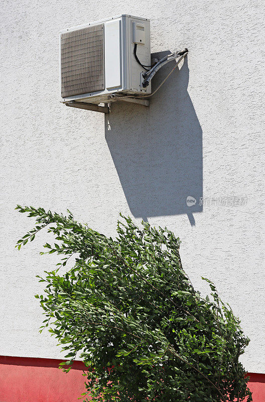 Air conditioner on the wall above a green bush